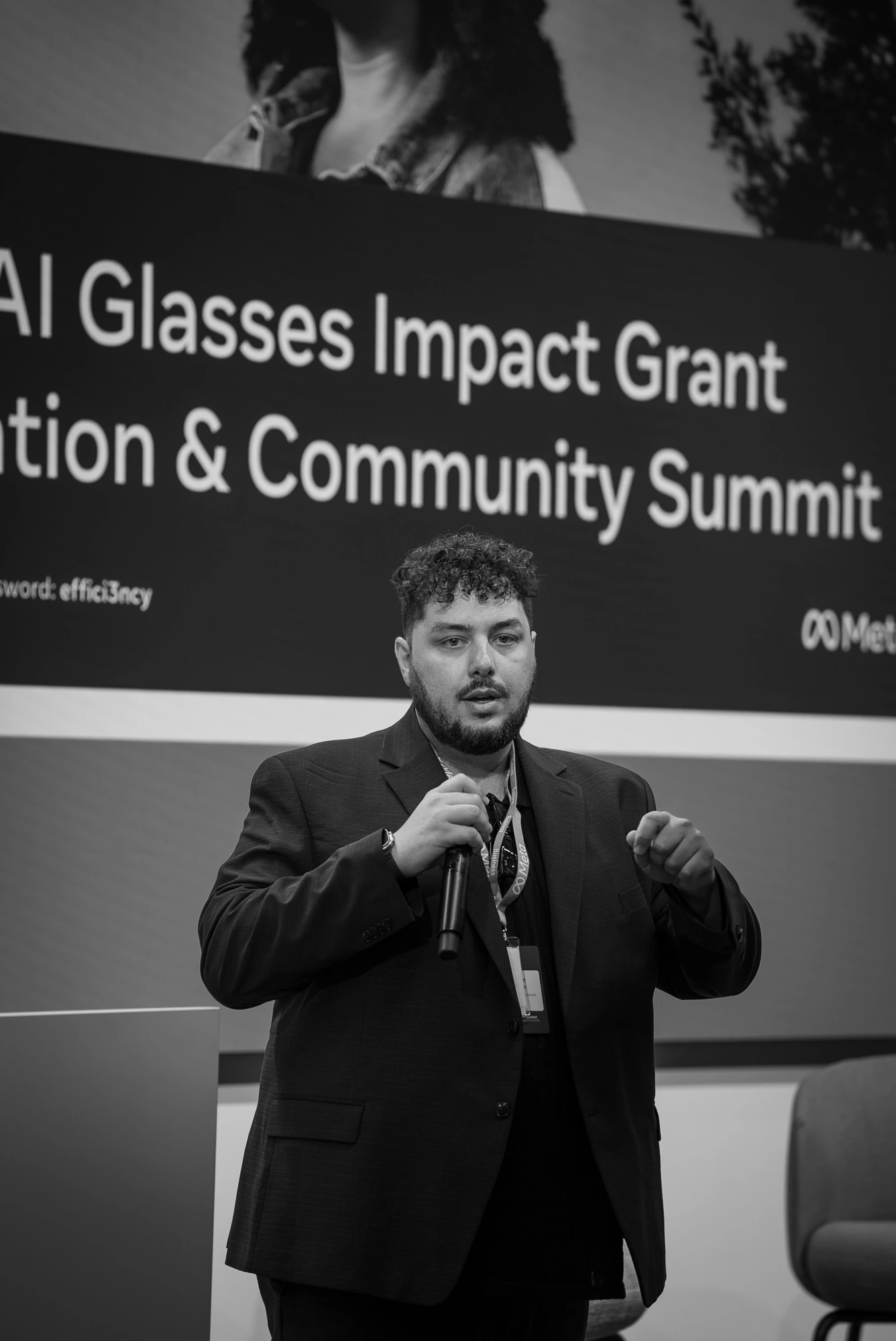 Black-and-white photograph of Trust Carbon founder Brayon Pieske speaking at Meta's AI Glasses Impact Grant Celebration and Community Summit, the Meta summit branding visible behind him