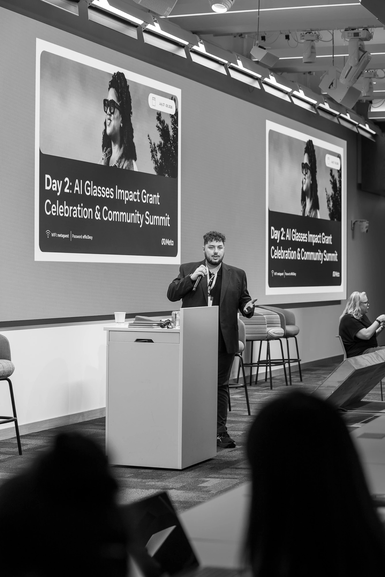 Black-and-white photograph of Trust Carbon presenting at the podium during Meta's AI Glasses Impact Grant Community Summit